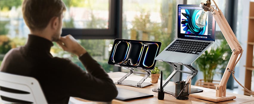 Mann arbeitet am Schreibtisch mit Laptop und Tablet auf Wozinsky verstellbarem Ständer in hellem Büro am Fenster