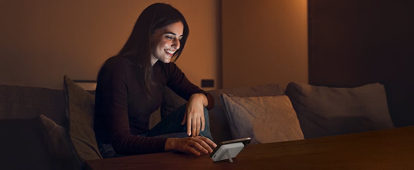 Frau lächelt beim kabellosen Laden ihres Smartphones mit Wozinsky Powerbank auf dem Tisch in gemütlichem Abendlicht