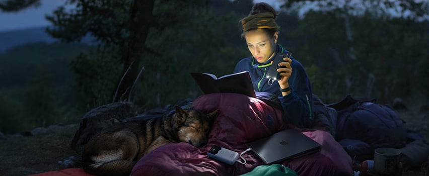 Frau liest Buch im Zelt mit Hund und lädt Smartphone und Laptop mit Wozinsky Powerbank und Stirnlampe