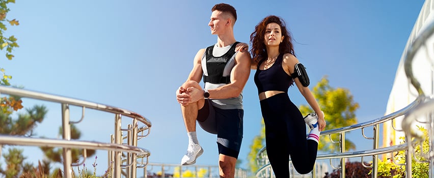 Paar trainiert draußen in Sportkleidung mit Wozinsky Gewichtsweste und Lauf-Armband für Smartphone an sonnigem Tag